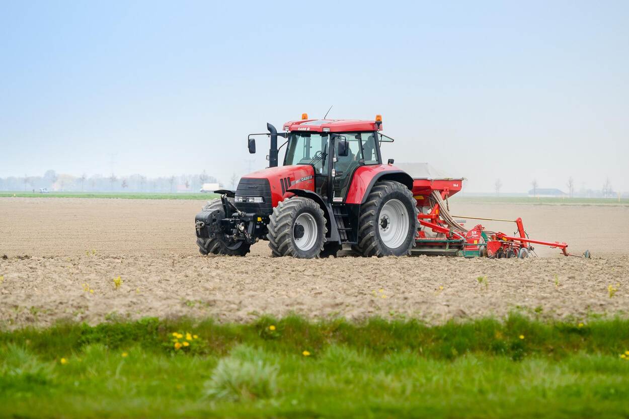 Boer bewerkt met rode tractor de akker